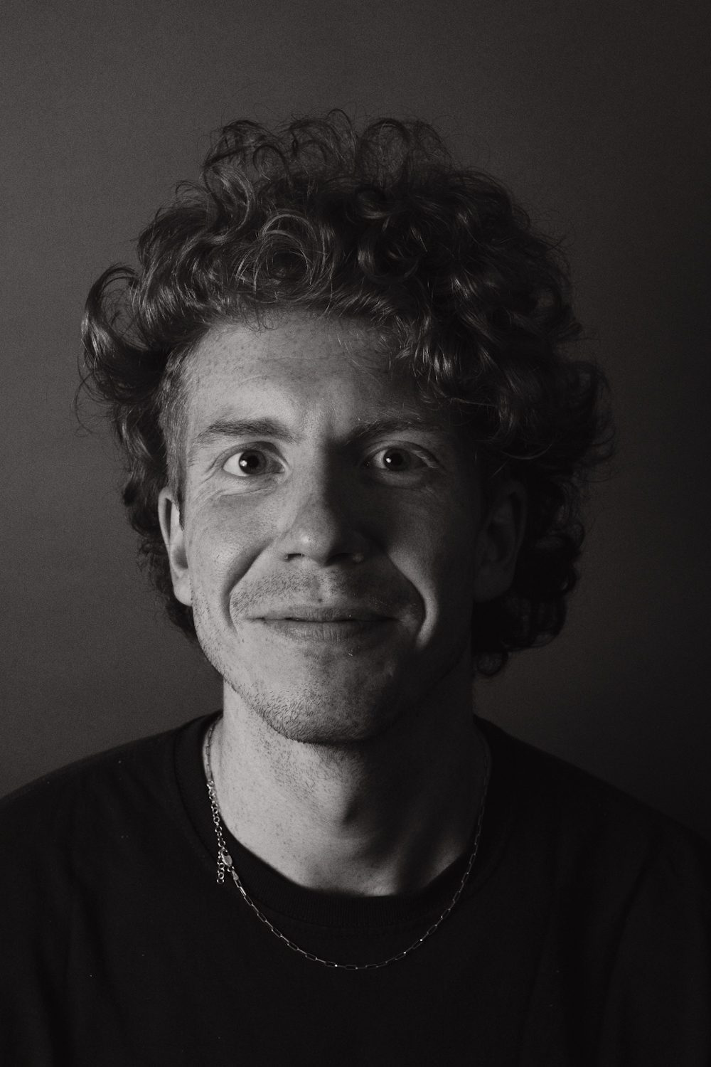 Black and white close-up portrait, subject with curly hair and a small smile.
