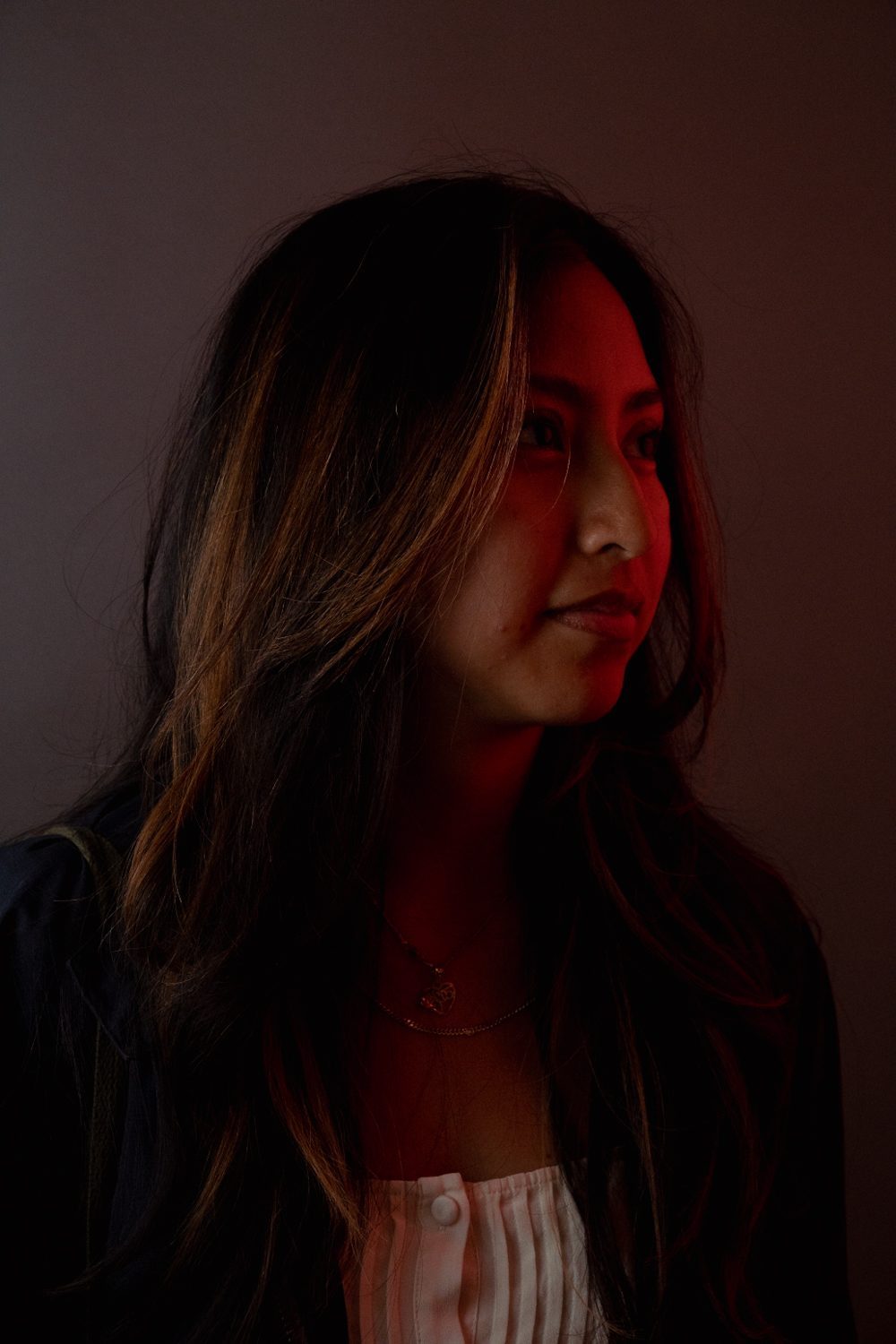 Studio portrait lit with a red gel, subject with long dark hair looking off camera.