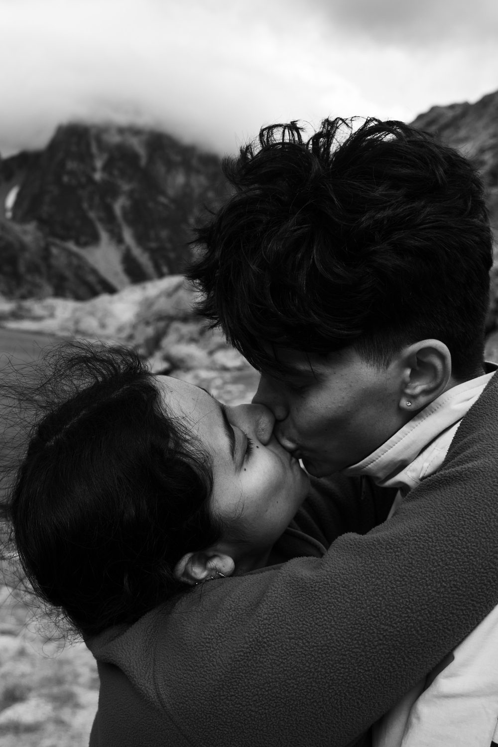 Black and white outdoor portrait, two people close together, one kissing the other's cheek.
