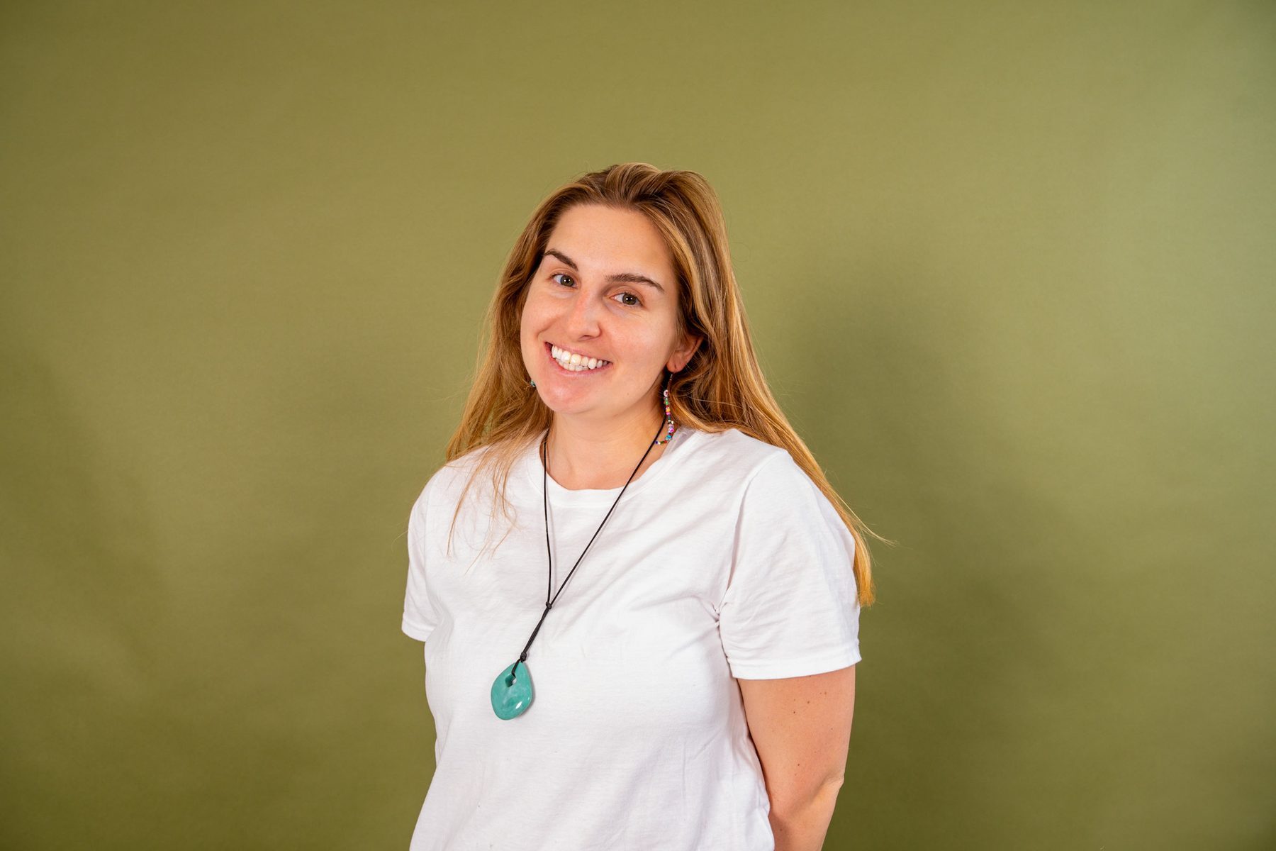 Alyssa Caples, standing against an olive backdrop in a white t-shirt.