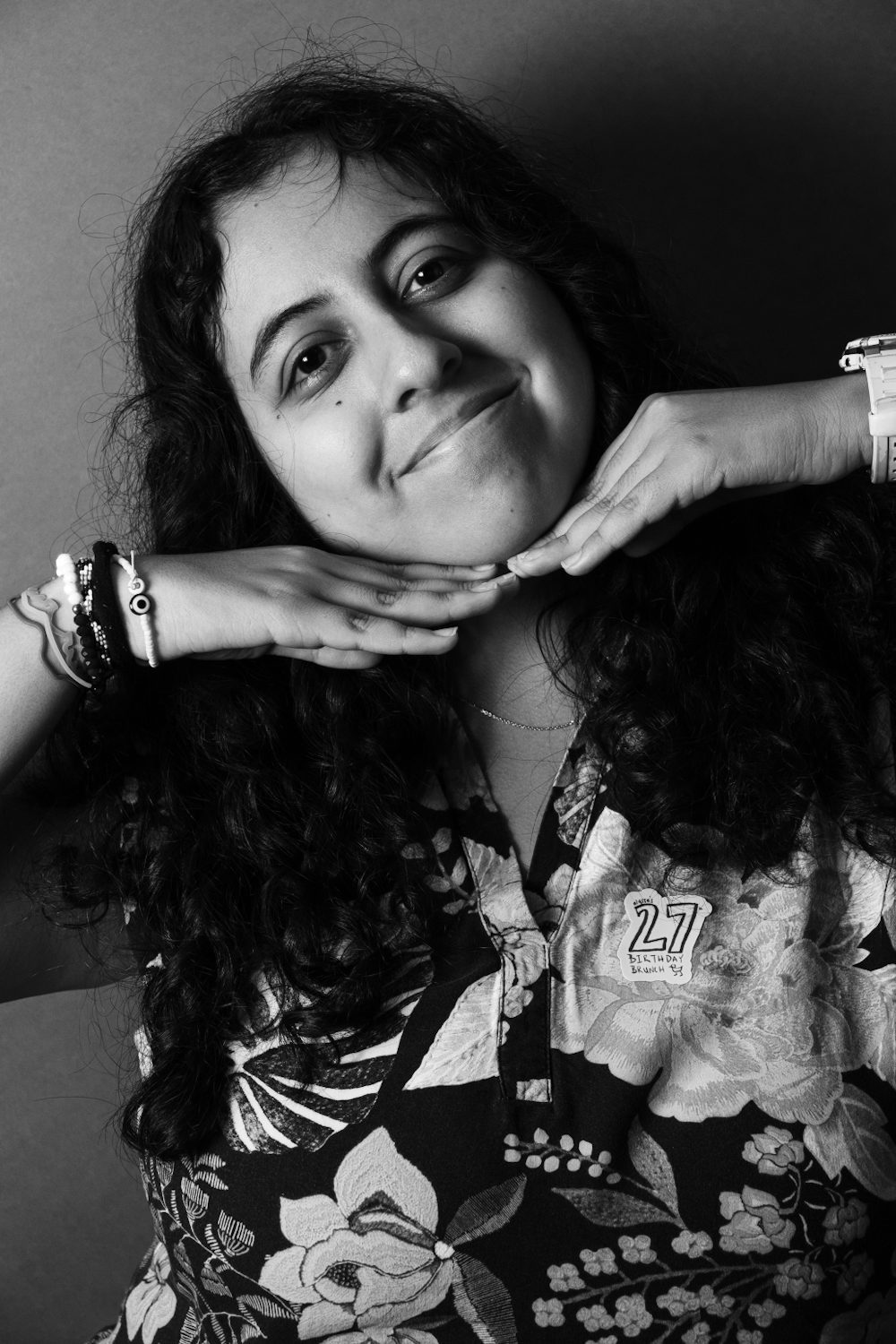 Black and white portrait, subject resting their chin on stacked hands, smiling.