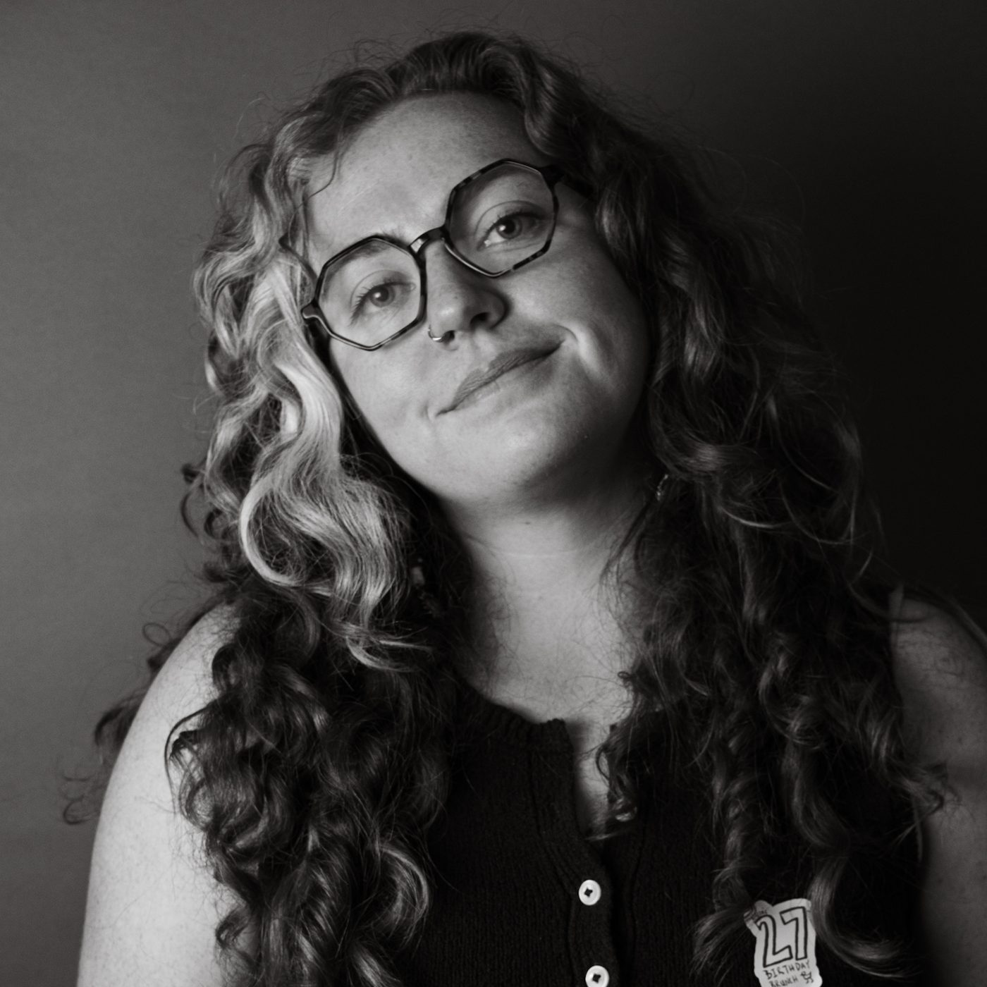 Black and white close-up, subject with long curly hair and round glasses.
