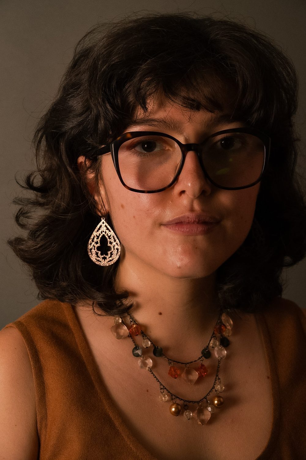 Tight studio close-up, subject in glasses with a large drop earring.