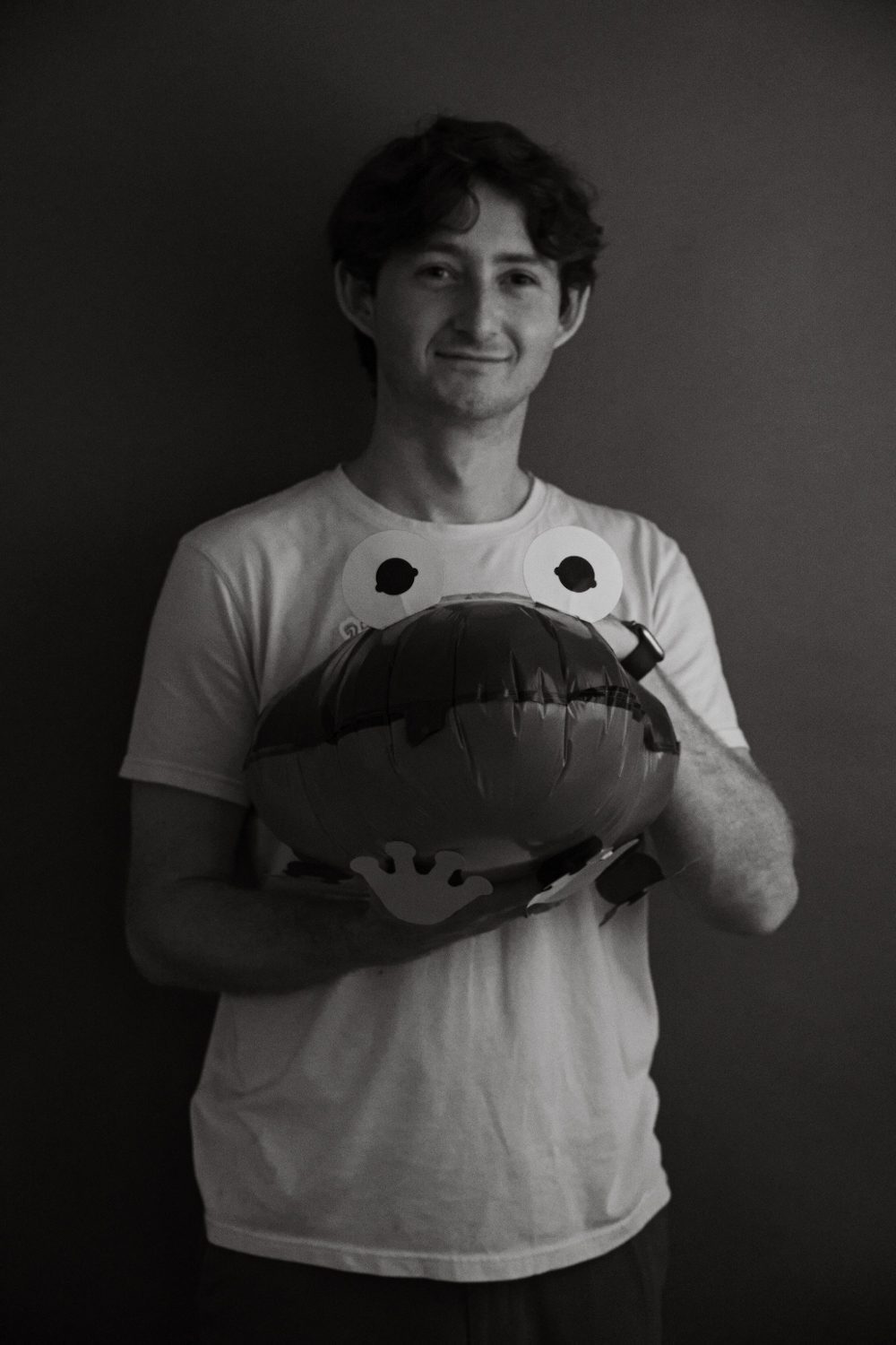 Studio portrait, subject standing and holding a large round cushion at their waist.