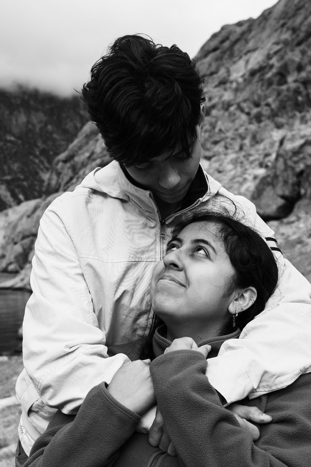 Black and white outdoor portrait, one person leaning back against the other and looking up at them.
