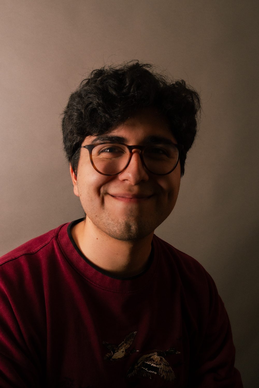Studio close-up, subject smiling in glasses and a maroon sweatshirt.