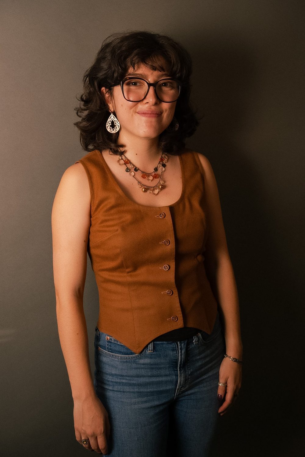 Studio portrait, subject standing in an ochre waistcoat and jeans.