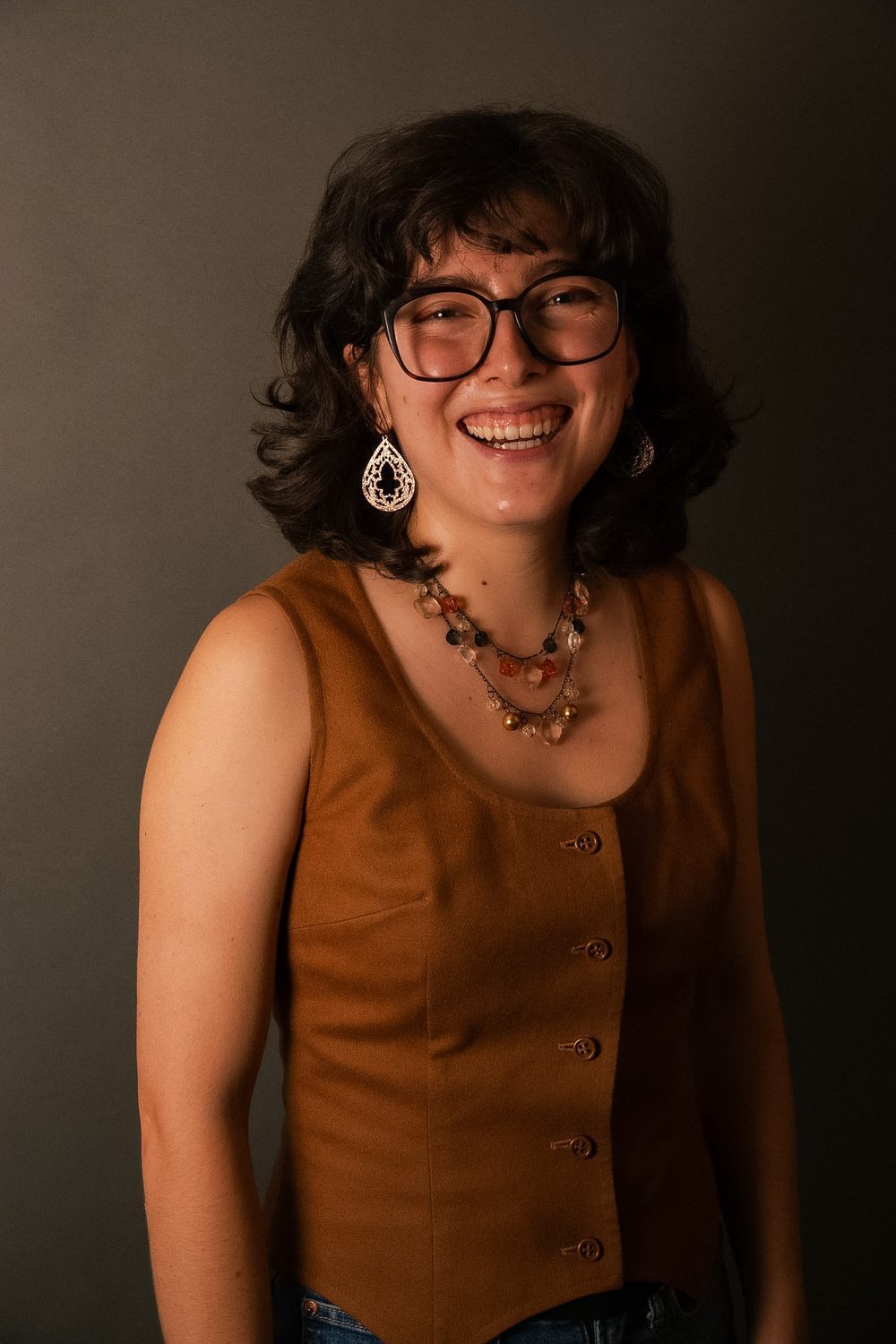 Studio portrait, subject laughing, in an ochre waistcoat and beaded necklaces.