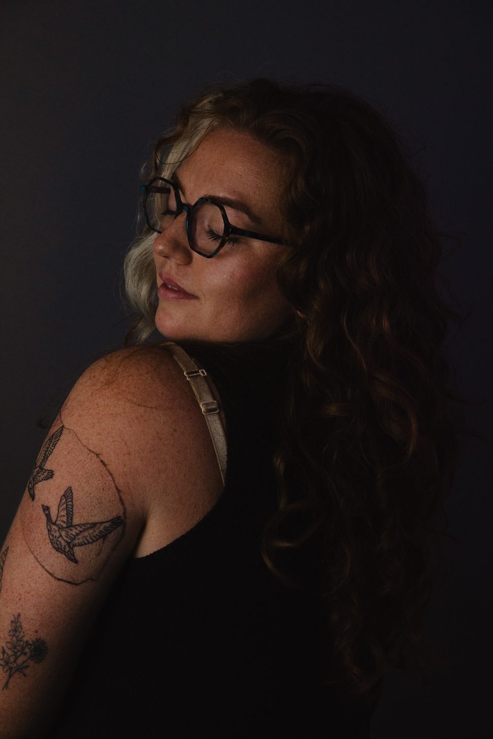 Low-key portrait in profile, warm light falling across a tattooed arm.