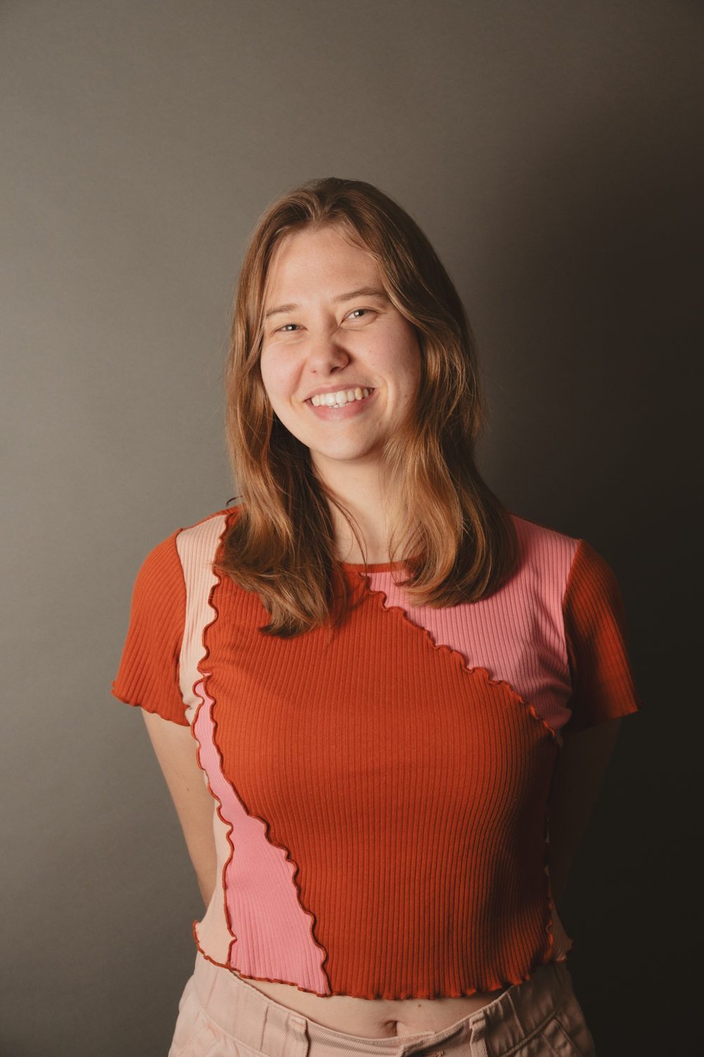 Studio portrait on a warm brown backdrop, subject smiling in a red and pink top.